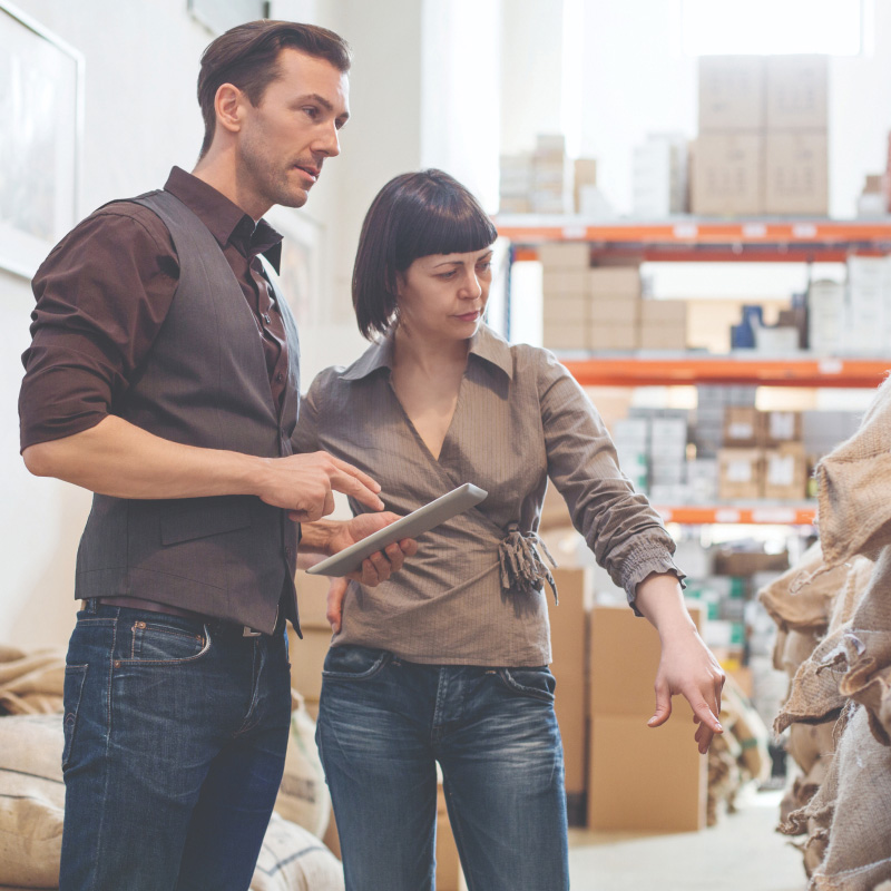 Two professionals standing in a warehouse reviewing stock